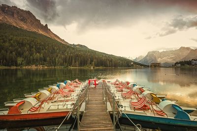 Boats moored at lake misurina by mountains against cloudy sky during sunset