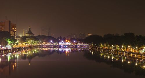 Illuminated buildings by river against sky at night