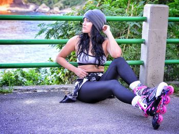 Young woman wearing roller skates while leaning on green railing of bridge