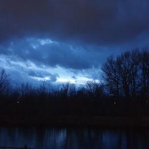 Silhouette trees by lake against sky at night