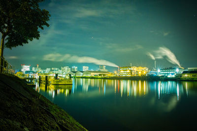 Illuminated city by river against sky at night