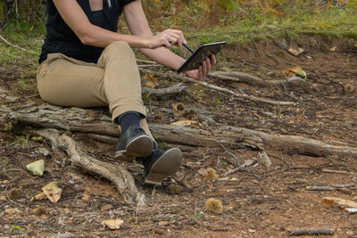 Low section of woman with digital tablet sitting in forest