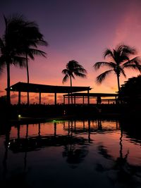 Silhouette palm trees by swimming pool against sky during sunset