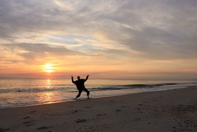 Silhouette people on beach against sky during sunset