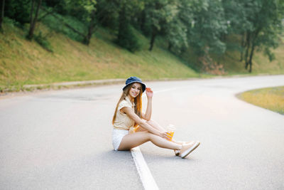 A happy girl in white shorts and a yellow blouse holds a glass of juice with a straw in her hands