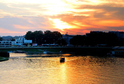 Scenic view of river by buildings against orange sky