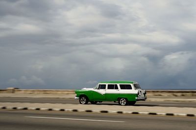 Vintage car on road against cloudy sky