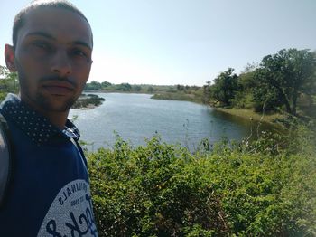 Portrait of young man standing by lake against sky