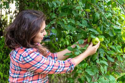 Side view of a young woman holding fruit growing in farm