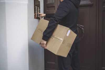 Midsection of delivery man ringing bell to deliver package at doorstep