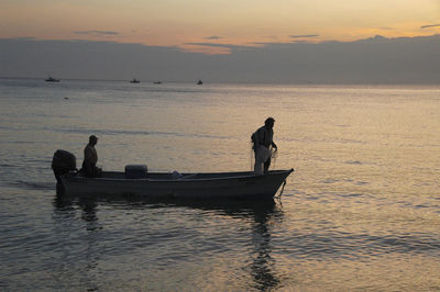 Silhouette men on boat in sea against sky