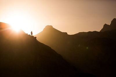 Back view of unrecognizable female traveler silhouette sitting on edge of cliff and admiring picturesque mountains in morning in pyrenees