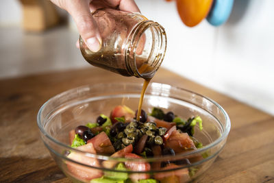 Close up of woman hands pouring dressing over a salad.