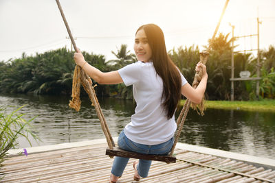 Full length of woman sitting by lake against sky