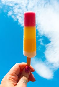 Cropped hand of woman holding flavored ice against blue sky during summer