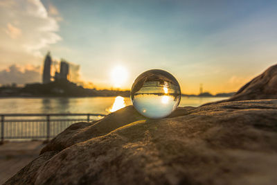 Reflection of crystal ball on water against sky during sunset