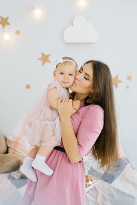 A young caucasian mother kisses her one year old daughter on the cheek at home