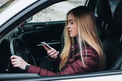 Young woman using smart phone in car