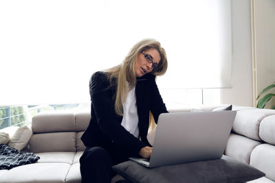 Businesswoman using laptop while talking on mobile phone at home