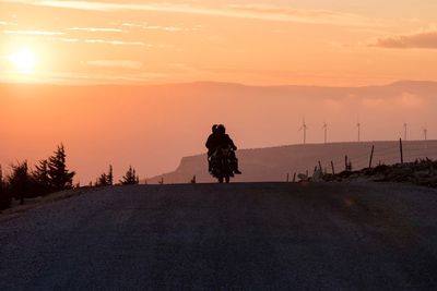 Silhouette people on motorcycle against sky during sunset