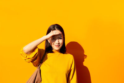 Portrait of woman shielding eyes against yellow wall