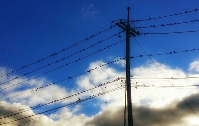 Low angle view of electricity pylon against cloudy sky