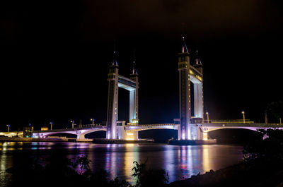 Illuminated bridge over river against sky at night