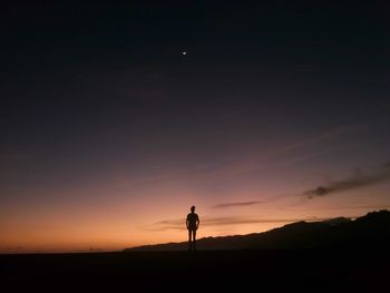 Silhouette man standing on field against sky during sunset