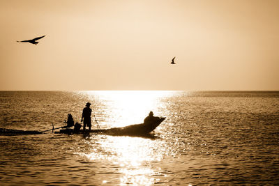 Silhouette men fishing in boat over sea against clear sky