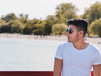 Young man wearing sunglasses while standing against sea