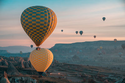 Hot air balloons flying over mountain against sky during sunset