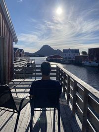 Rear view of man sitting on seat against sea and sky