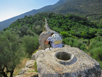 Woman looking into rock hole against mountains