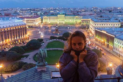 Portrait of young woman against cityscape at dusk