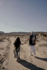 Rear view of woman walking at desert against sky