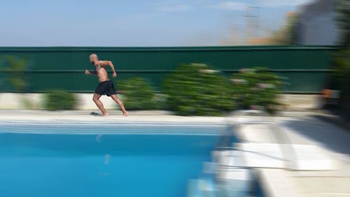 Side view of shirtless man running at poolside