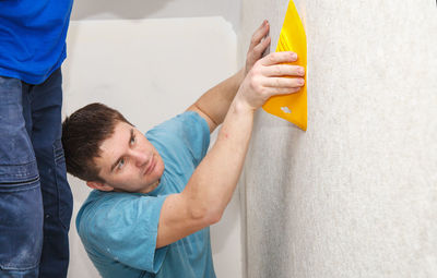 Side view of painter putting wallpaper on wall at construction site