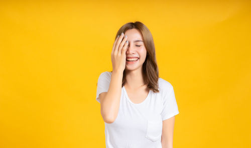 Beautiful young woman standing against yellow background