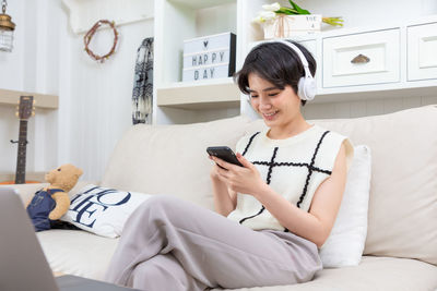 Young woman using digital tablet while sitting on bed at home