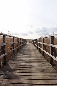 Wooden footbridge on boardwalk against sky