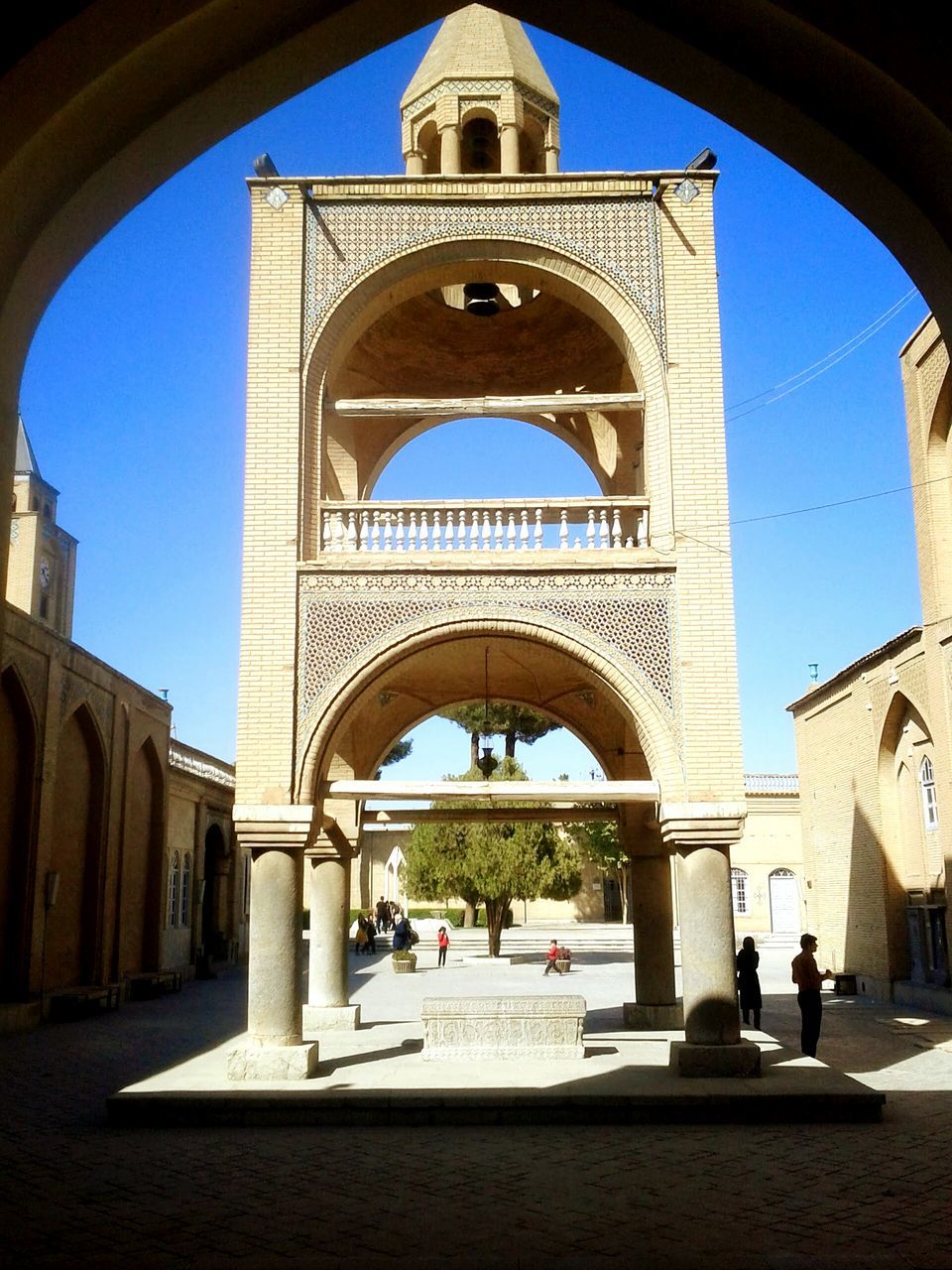 arch, architecture, built structure, building exterior, clear sky, blue, archway, entrance, sunlight, history, arched, day, travel destinations, incidental people, walking, shadow, person, place of worship, men