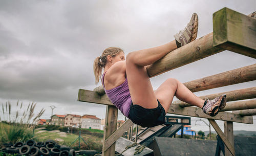 Low angle view of woman exercising on wooden planks against sky