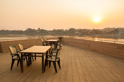 Empty chairs by swimming pool against sky during sunset