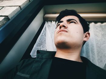 Low angle view of thoughtful young man looking away while standing at doorway