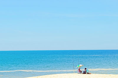 Men standing on beach against clear blue sky