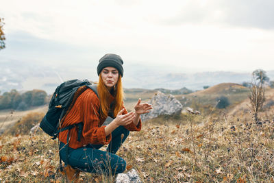 Full length of young woman sitting on mobile phone against sky