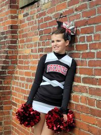 Portrait of a cheerleader standing against brick wall