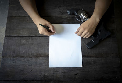 Close-up of businessman writing in paper with gun on table 