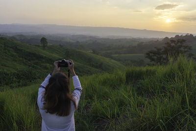 Rear view of woman on landscape against sky during sunset