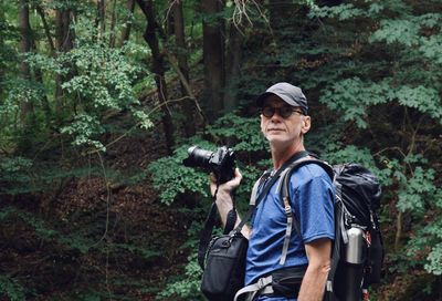 Man looking away while holding camera in forest